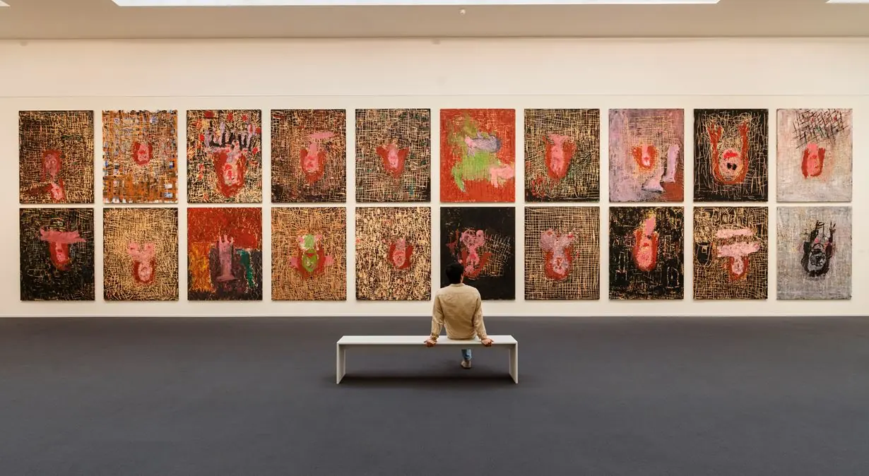 Visiteur assis face a un mur de toiles dans une salle d exposition
